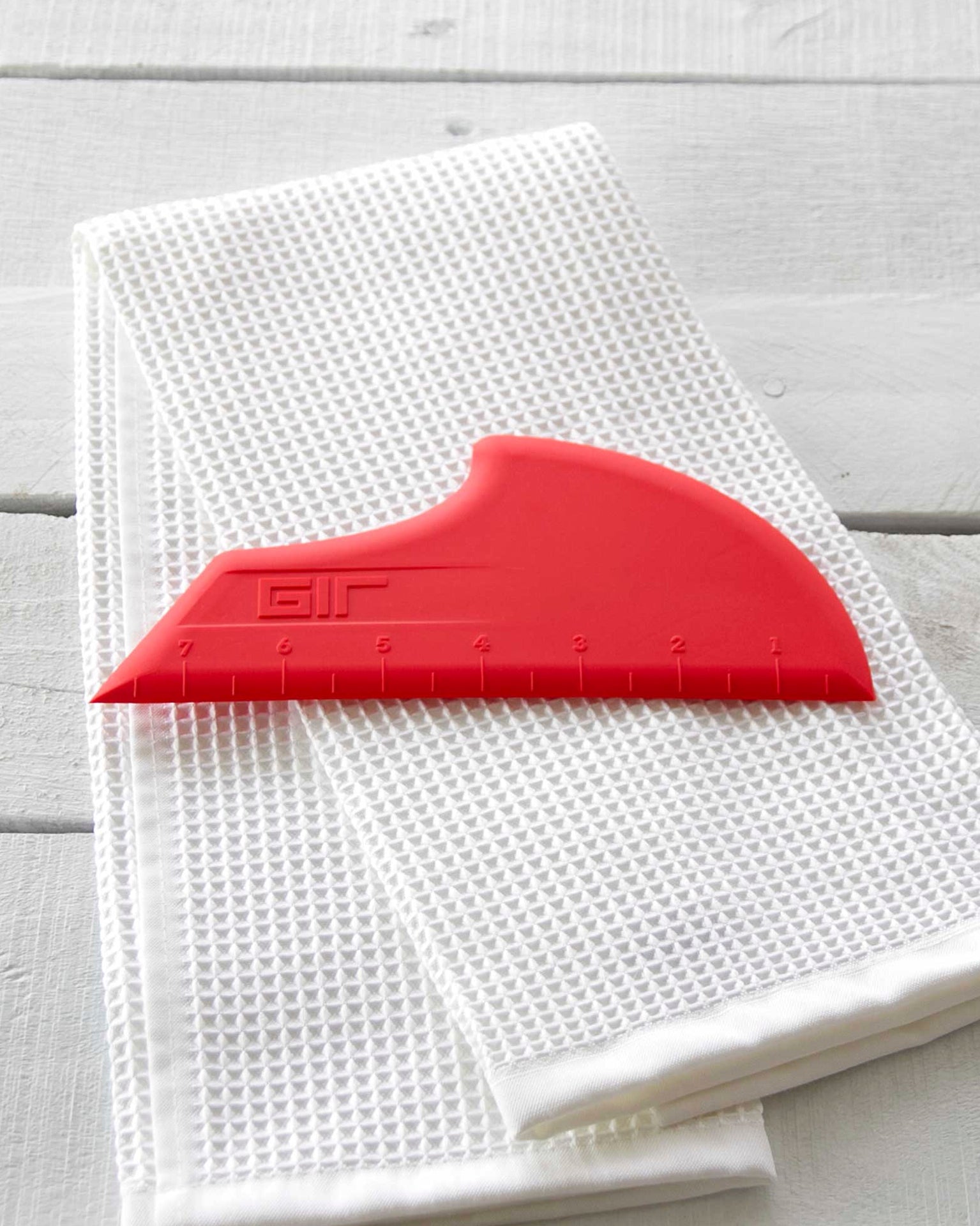 The GIR Scraper in Red resting on a white towels. 