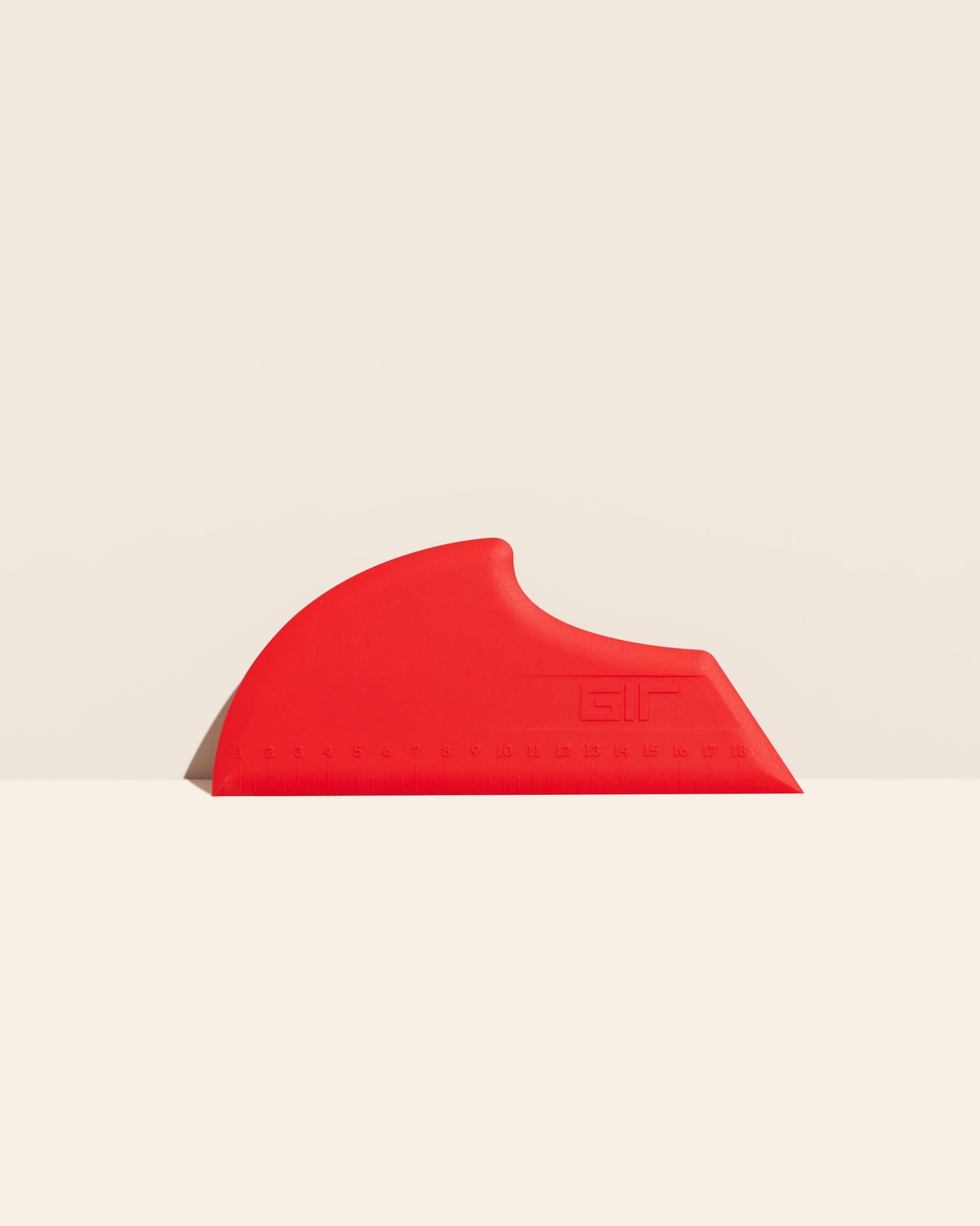 The GIR Scraper in Red on a cream background. 